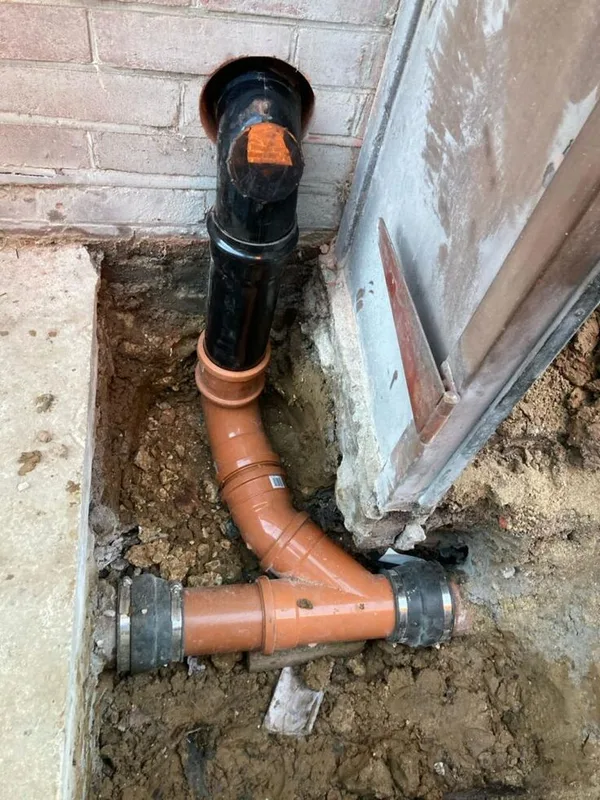 New orange PVC drainage bend and pipe connected to a soil stack in an open trench (illustrative image)