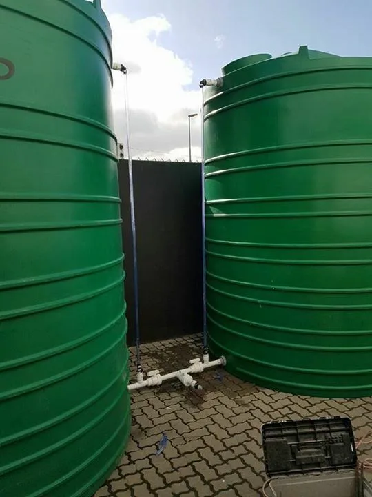 Two large green water tanks joined by a white pipe manifold with isolating valves (illustrative image)