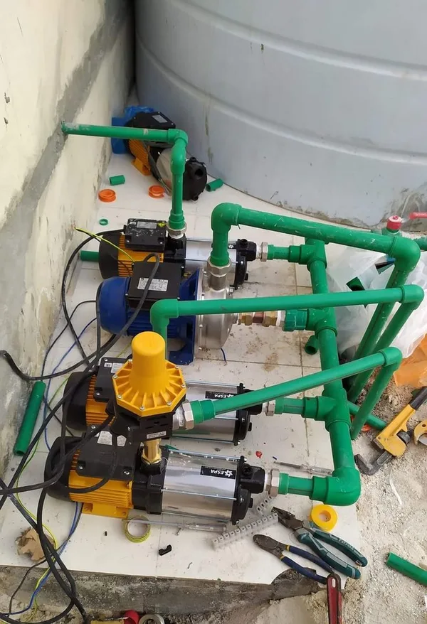 Booster pumps connected to a water tank with green PPR pipework and a pressure controller (illustrative image)