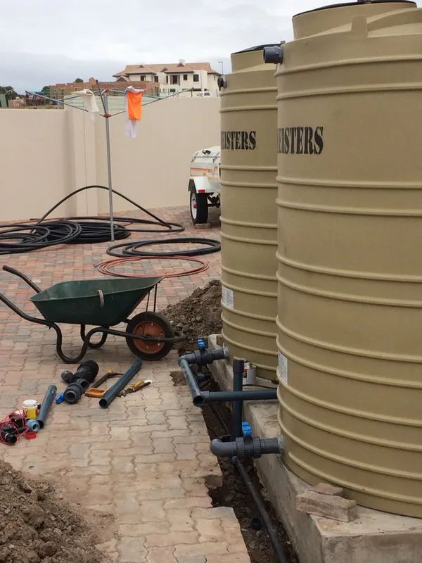 Two water storage tanks on a concrete base being connected with outlet pipework (illustrative image)
