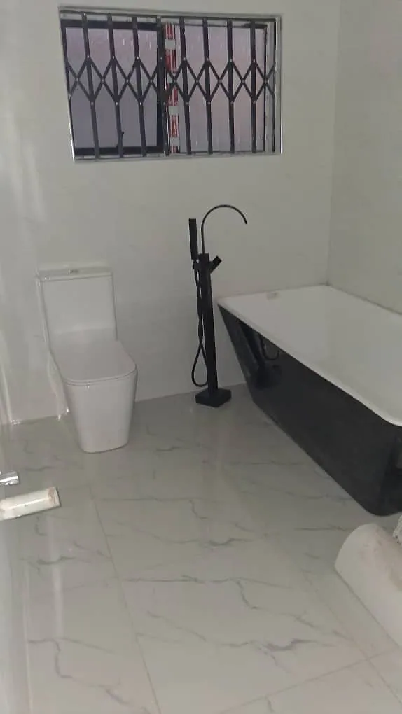Bathroom with white marble-effect floor and wall tiles, a black freestanding bath, floor mixer and close-coupled toilet