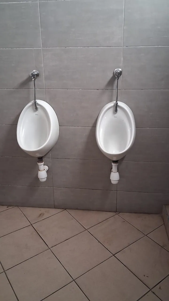Two wall-hung urinals with flush valves and waste traps installed on grey wall tiles