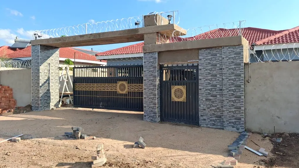 Entrance pillars and walls clad in grey stone-effect split tiles beside black steel gates
