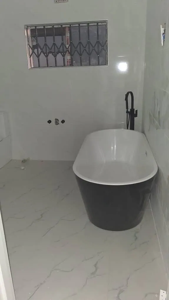 Floor-standing black bath mixer installed beside a freestanding bath on marble-effect floor tiles