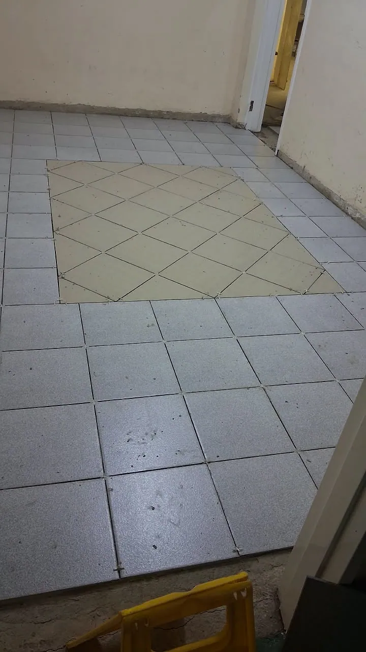 Floor tiling in progress with a diagonal feature panel set into square grey tiles