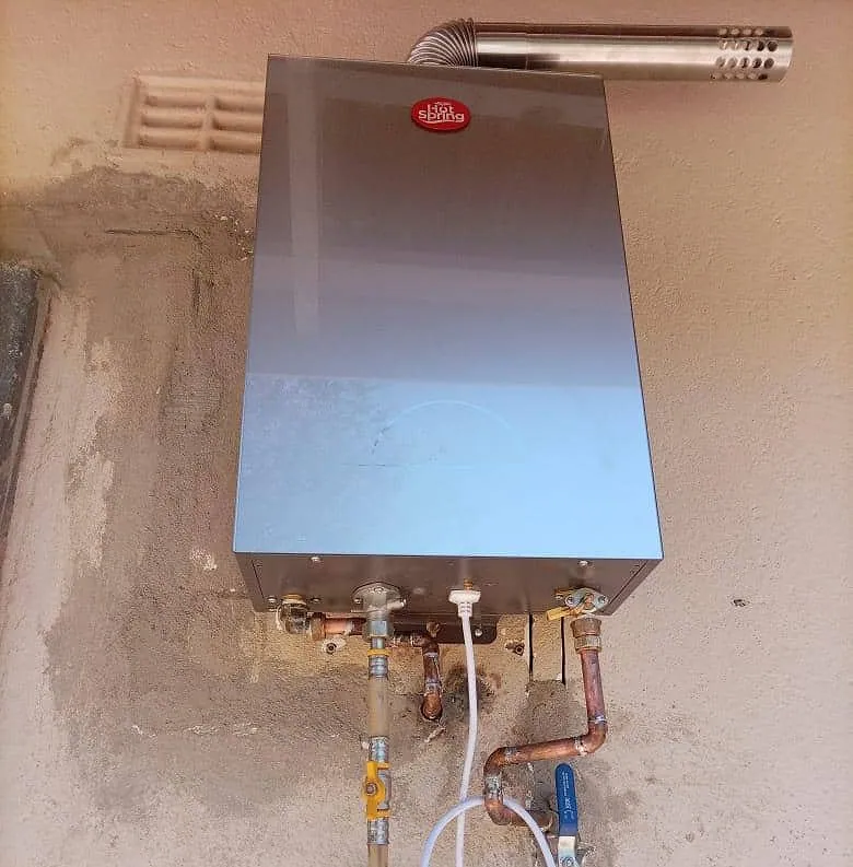 Wall-mounted gas water heater connected with copper pipework, isolating valves and a flue