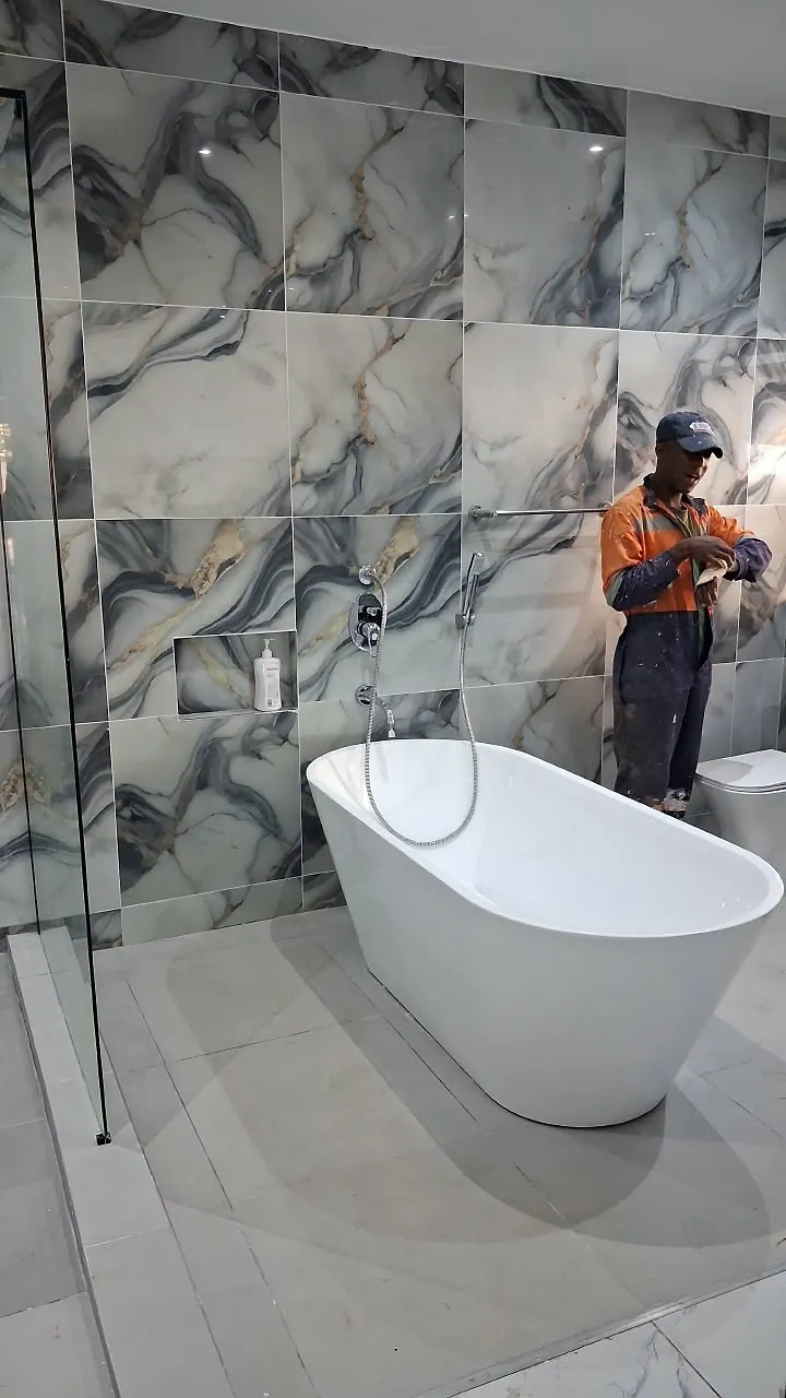 Freestanding bath, wall-mounted shower mixer and large marble-effect wall tiles in a bathroom finished by MAINLINE, with a team member on site